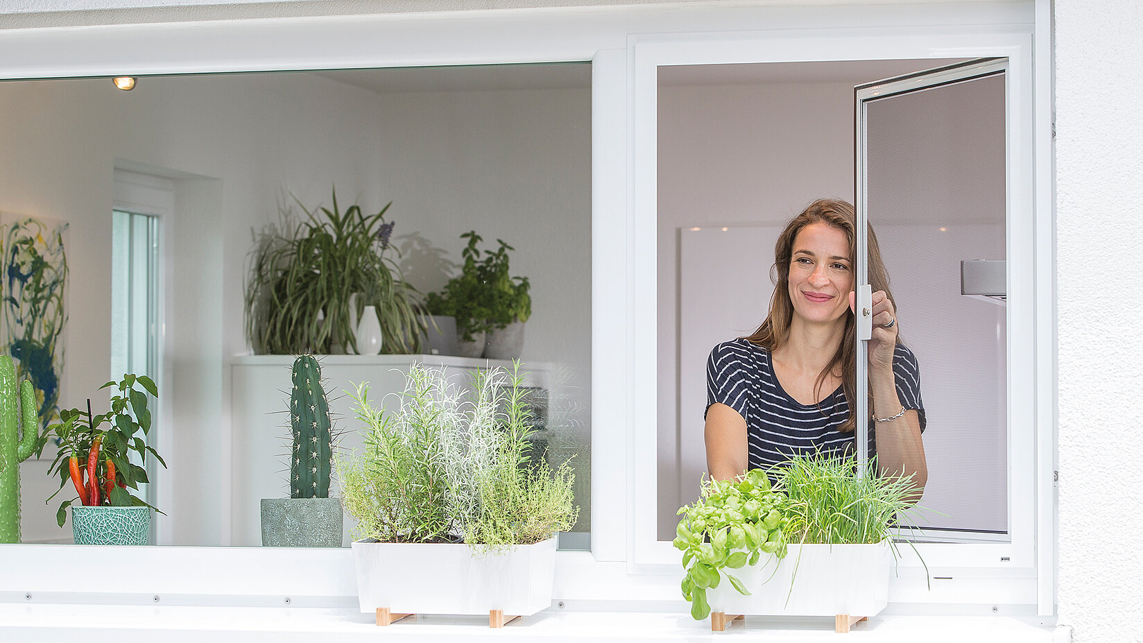 Frau öffnet Insektenschutz-Drehfenster über einer Kräuterbank.
