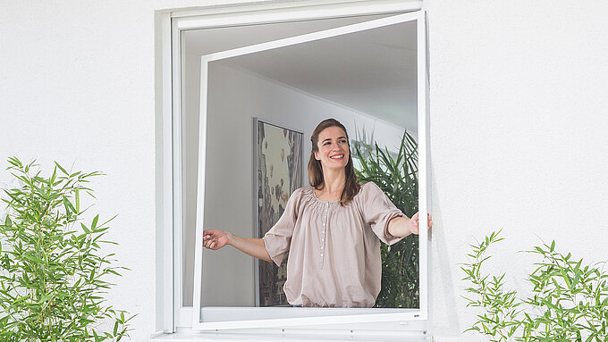 Frau hebt Insektenschutz mit Spannrahmen ans Fenster