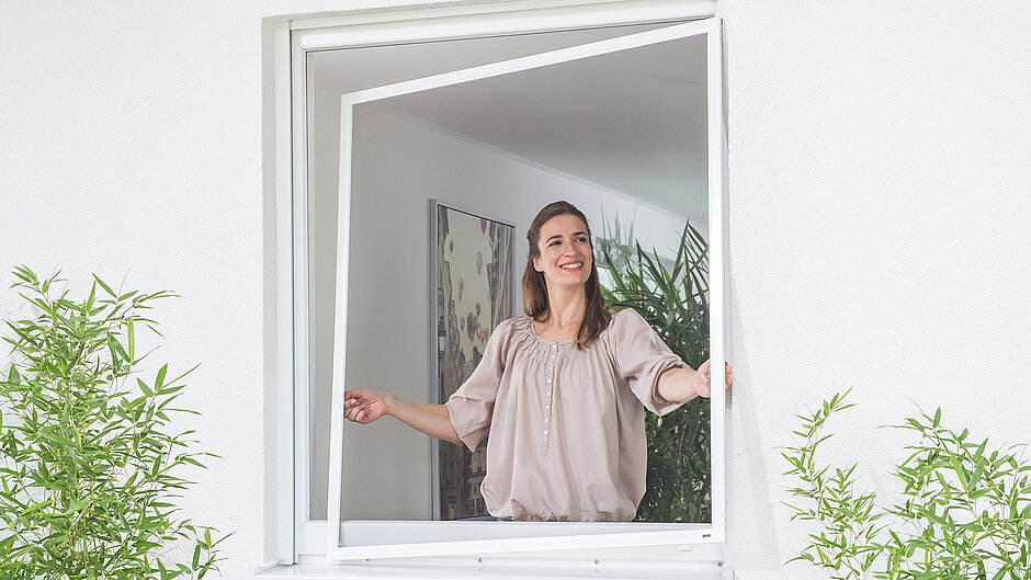 Frau hebt Insektenschutz mit Spannrahmen ans Fenster