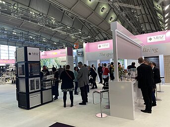 MHZ-Messestand mit mehreren Besuchern, Produktmustern und Beratungstheke auf einer Fachmesse für Sicht- und Sonnenschutz.