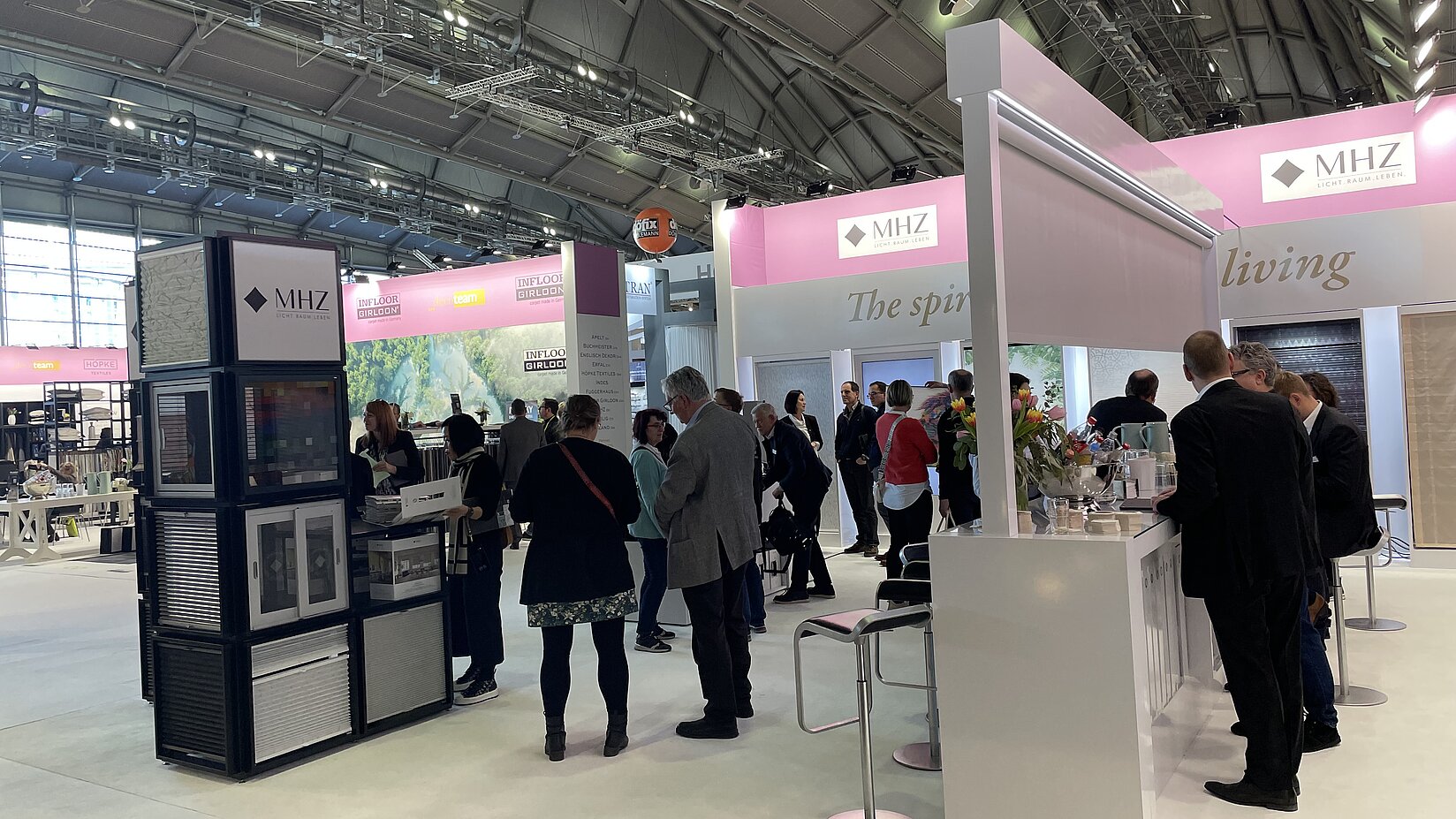 MHZ-Messestand mit mehreren Besuchern, Produktmustern und Beratungstheke auf einer Fachmesse für Sicht- und Sonnenschutz.