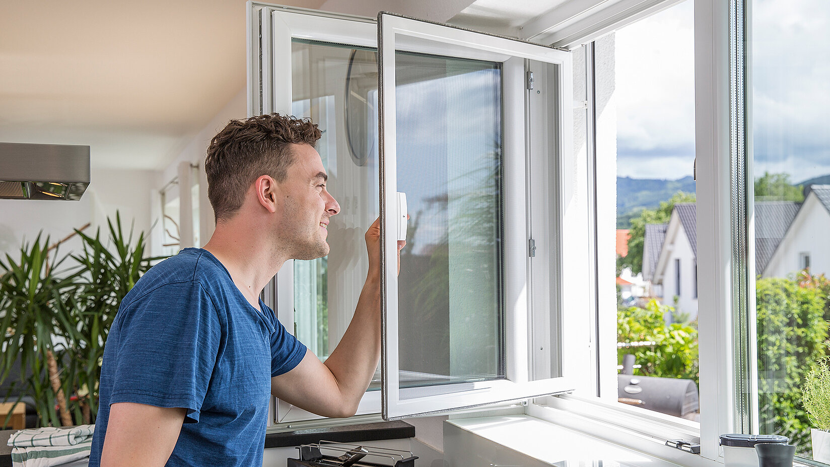 Mann öffnet ein Pendelfenster mit Insektenschutz in einem hellen Raum.