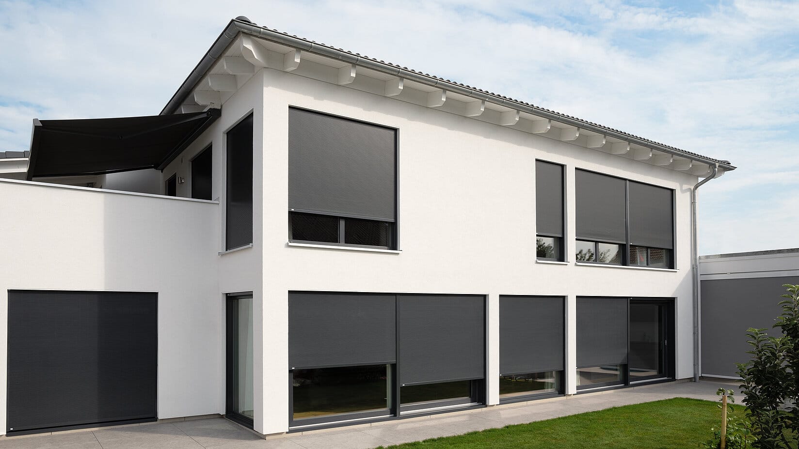 Gartensicht auf ein Haus mit Metallbehängen als Sonnenschutz