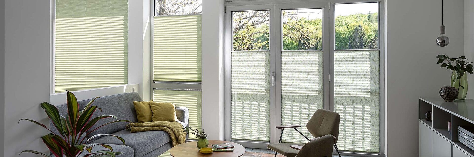 Modernes Wohnzimmer mit grossen Fenstern, ausgestattet mit halbtransparenten, grünen Plissees als Sicht- und Sonnenschutz.