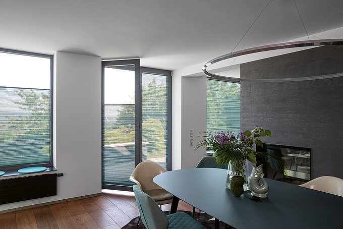 Elegante woon- en eetkamer met lichtdoorlatende plisségordijnen voor kamerhoge ramen. Plisségordijnen creëren een aangename lichtsfeer en bieden flexibele privacybescherming.