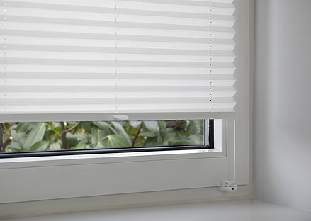 Weisses Plissee mit Klemmträger im Fensterrahmen montiert, Detailaufnahme der unteren Halterung.